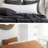 A close-up of a bed with dark gray and white linen pillows and bedding.
