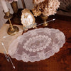 Elegant oval lace embroidered placemat displayed on a wooden table with decorative elements.