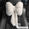 A white plush bowknot neck pillow is shown resting on a black car seat headrest.
