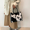A woman holds a black and white faux fur leopard print tote bag while wearing a beige coat and skirt.