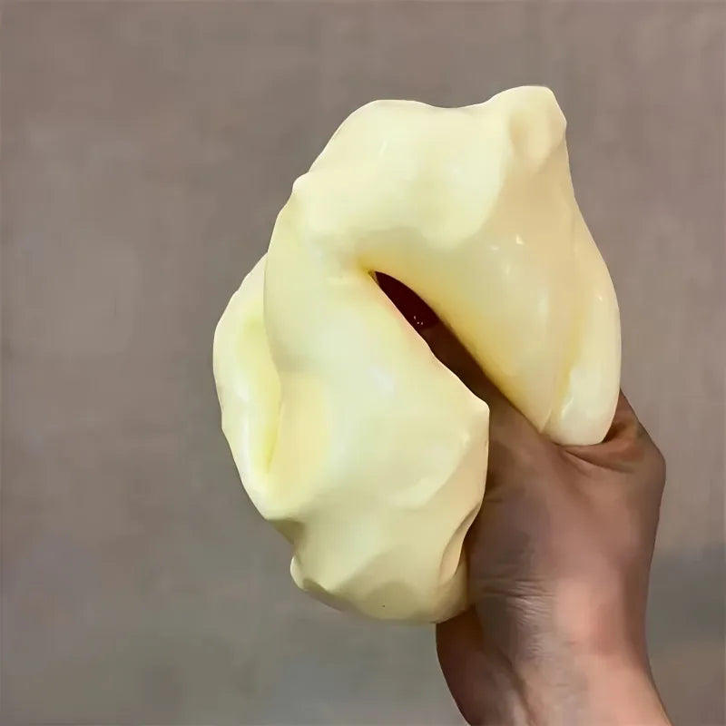 Eine Hand drückt ein großes, blassgelbes, käseförmiges, weiches Spielzeug.