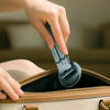 A hand is using a magnetic phone holder device to open a beige leather handbag.