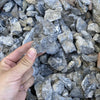A hand is holding a piece of natural grey aquarium stone amidst a pile of similar stones for aquascaping.