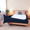 A dark navy stretch-fit box spring cover with an elastic edge is placed on a wooden bed frame.