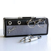 A vintage guitar amplifier with a black case and silver key holder attached, next to several guitar plugs.