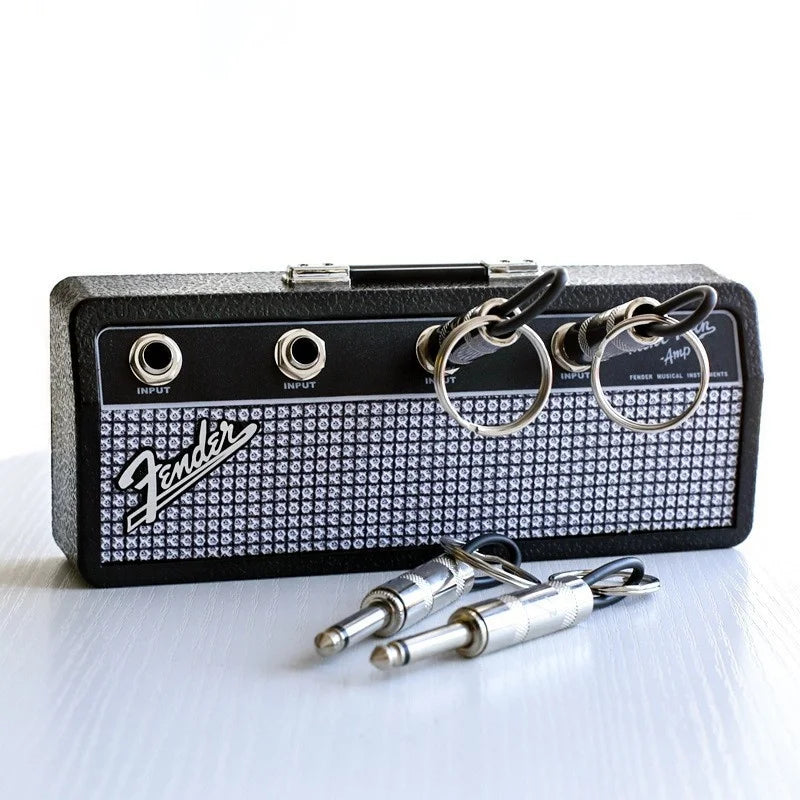 A vintage guitar amplifier with a black case and silver key holder attached, next to several guitar plugs.