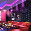 A modern interior featuring a dark geometric wallpaper with purple and pink light beams, illuminated by spotlights.