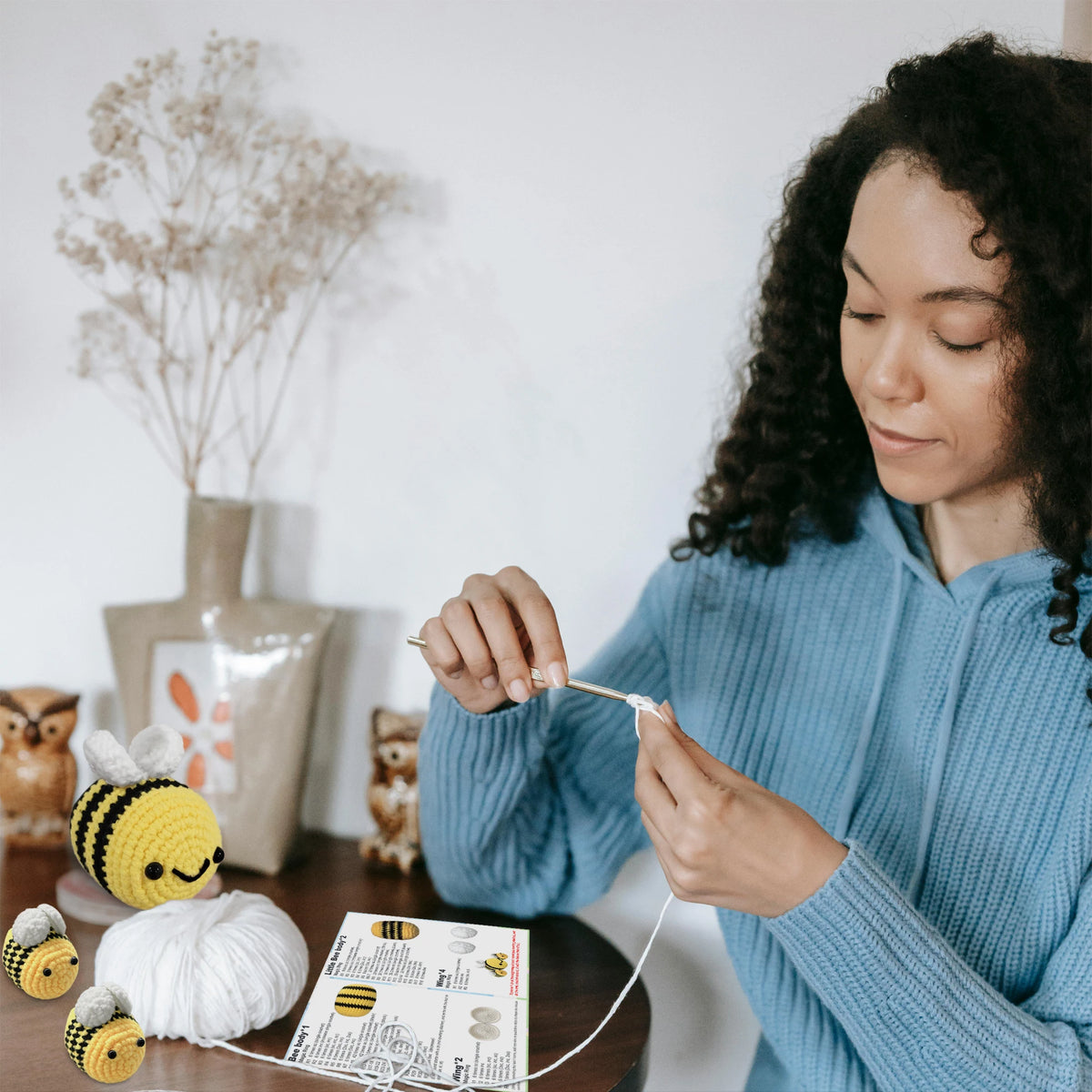 A person is using a beginner crochet kit with yarn and tools to create a small stuffed animal project.