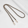 A close-up of a black and gold chain strap with a metal buckle laid diagonally on a white surface.
