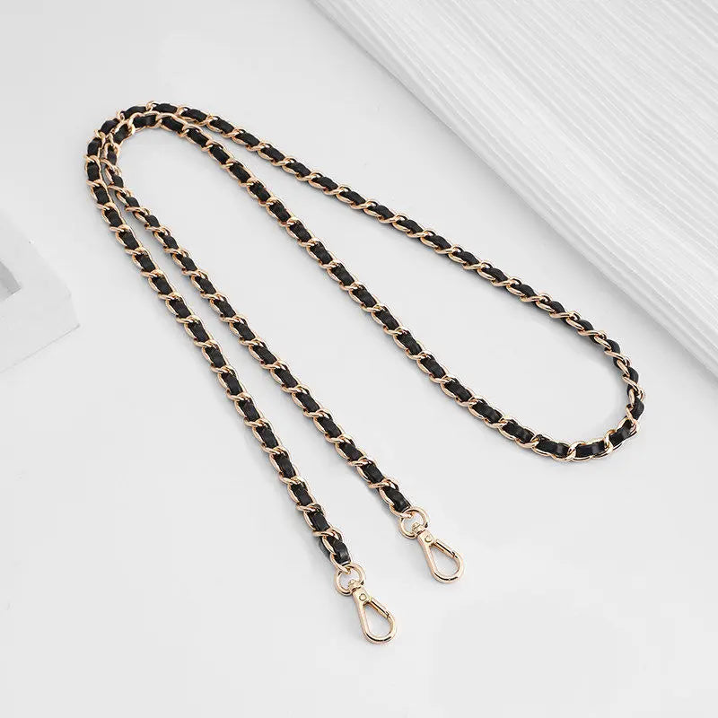 A close-up of a black and gold chain strap with a metal buckle laid diagonally on a white surface.