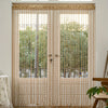 A pair of sheer beige curtains with long golden tassels covering a glass door or window.