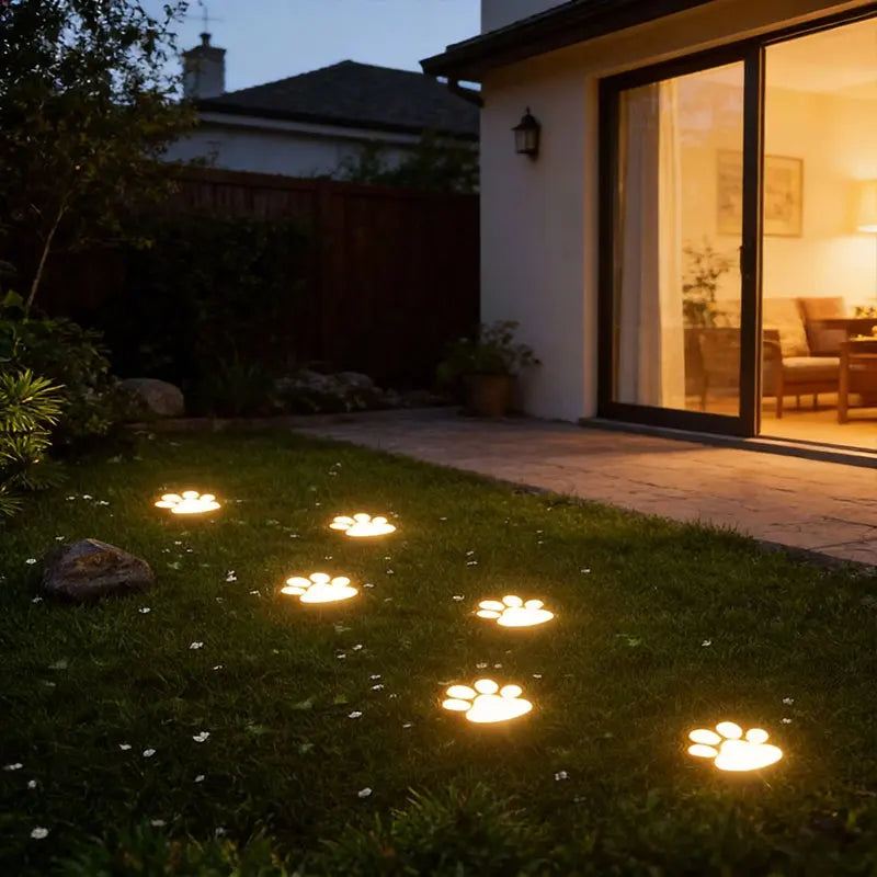 Four glowing solar dog paw lights illuminate a pathway in a grassy garden at dusk.