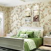 A bedroom featuring a bed with green linens and white headboard against a floral wallpaper backdrop.