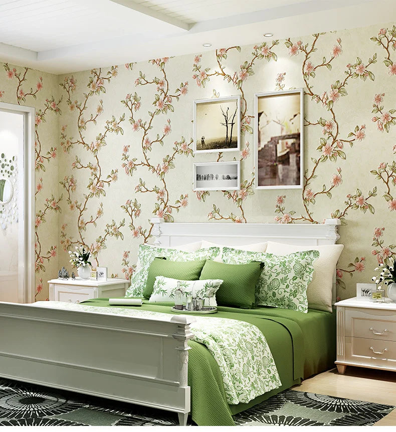 A bedroom featuring a bed with green linens and white headboard against a floral wallpaper backdrop.
