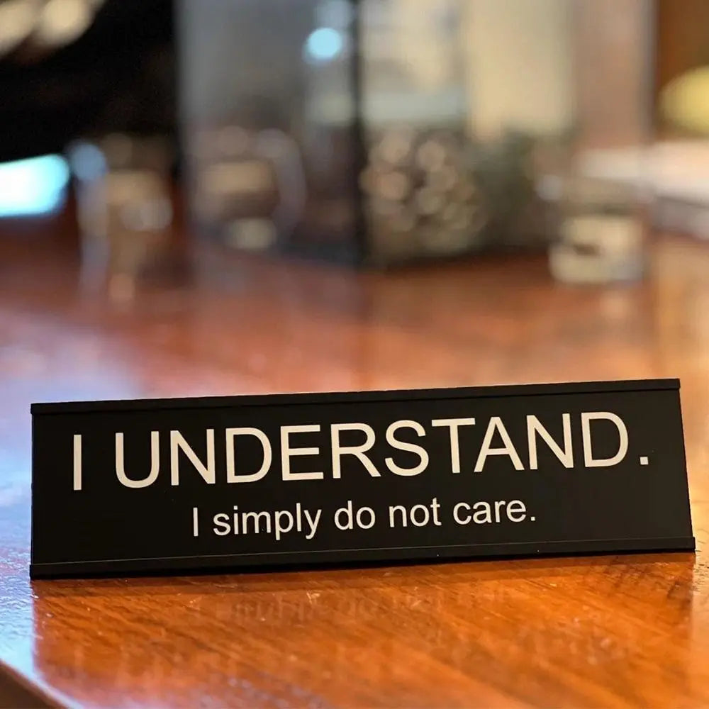 A black desk sign with white text that reads I UNDERSTAND I simply do not care.