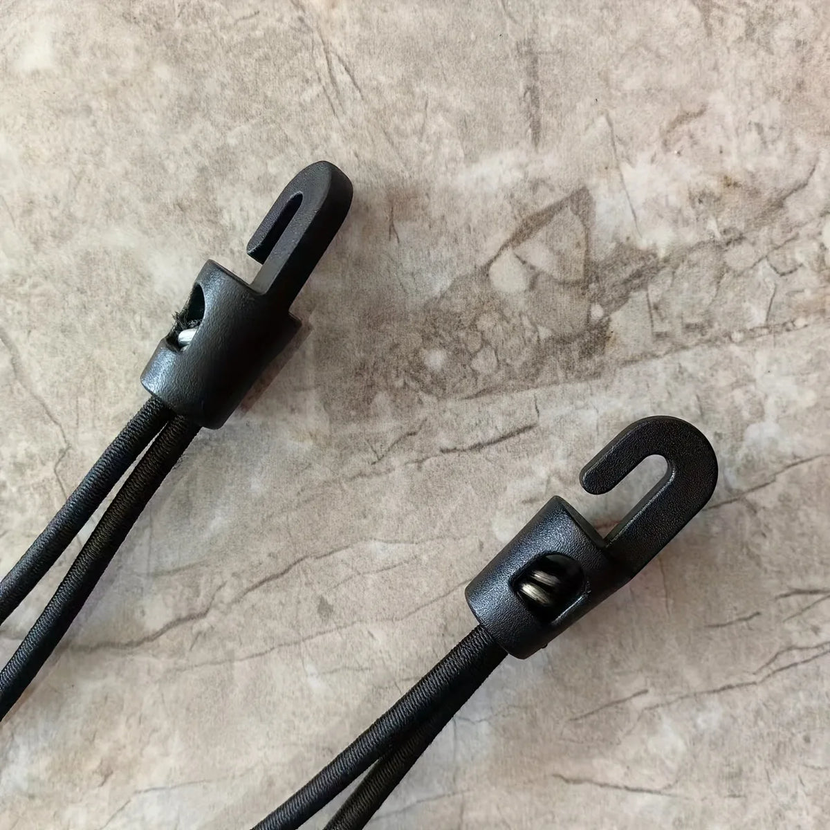 A close-up of a black heavy-duty elastic tie-down strap with metal hooks resting on a light marbled surface.