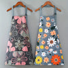 A floral print kitchen apron in gray featuring pink, yellow, and orange flowers with an adjustable neck strap and pockets.