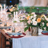 A wooden table set for an event with floral arrangements and glassware, featuring red placemats.