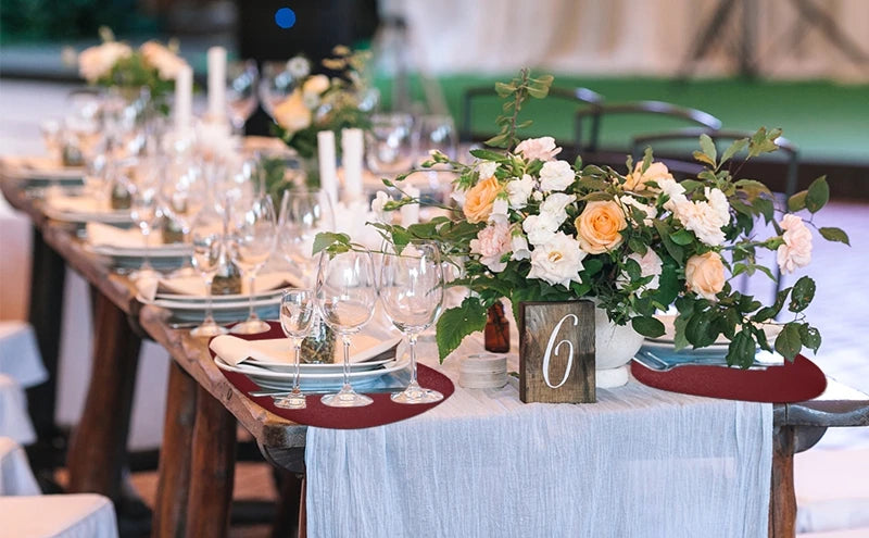 A wooden table set for an event with floral arrangements and glassware, featuring red placemats.