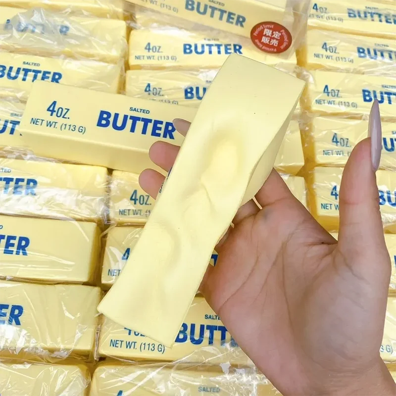 A hand holds a yellow butter stick fidget toy packaged in clear plastic bags.