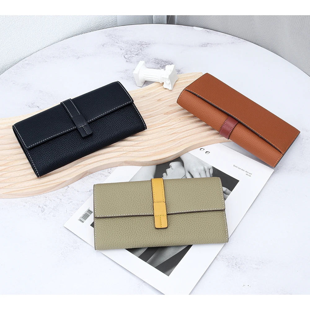 A display of three women's cowhide leather bifold wallets in black, brown, and olive green on a light wooden board.