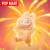 A fluffy, light brown Labubu plush doll with large eyes and a wide smile against an orange background.