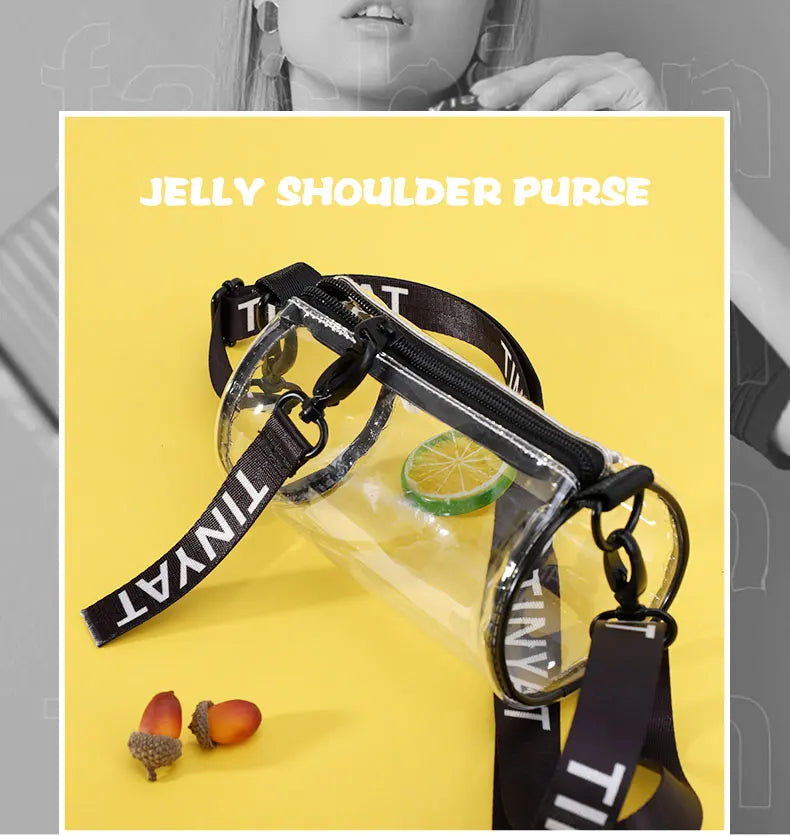 A clear jelly shoulder purse with a black strap and a lime slice, next to citrus fruit.