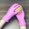 A hand wearing a pink disposable nitrile glove is holding a sesame seed bun sandwich.