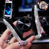 A hand holds a crystal air vent car phone holder with a black grip and a sparkling crystal phone attached.