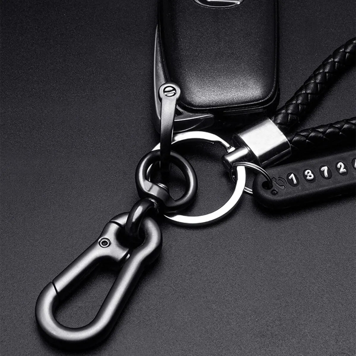 A close-up shot of a black personalized phone number keychain with a silver ring and braided leather rope.
