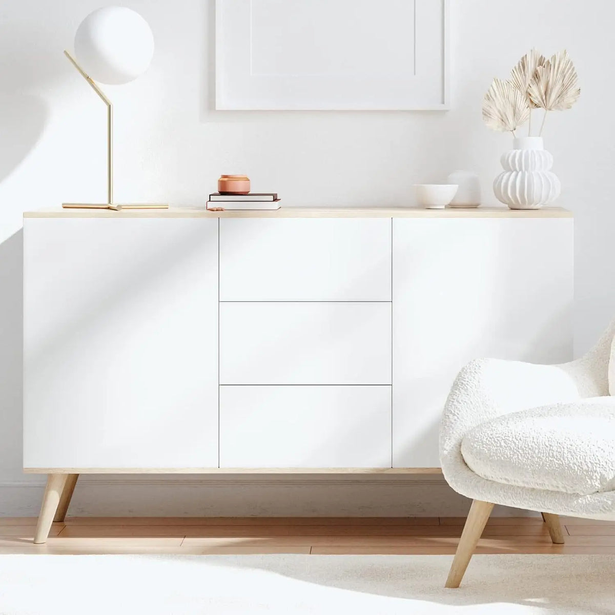 A white wooden cabinet with a light wood top and drawers, decorated with minimalist decor and natural light.