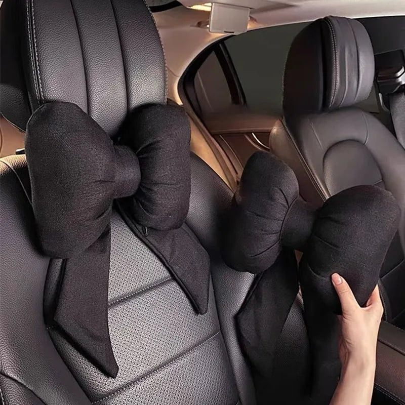 A black butterfly bow tie neck pillow with a fabric cover is shown in the interior of a car seat.