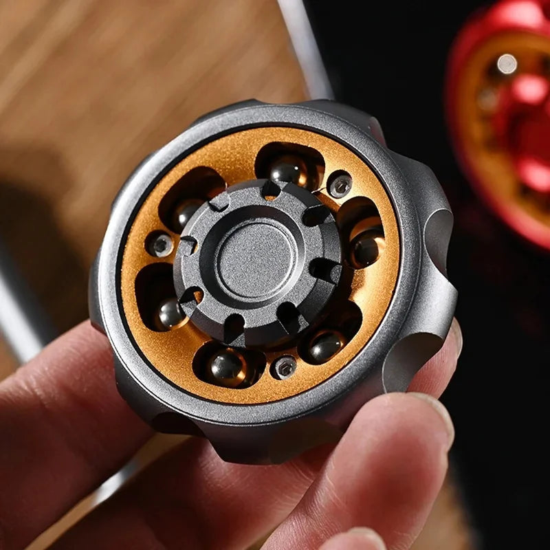 A hand holds a metal fidget toy with a silver outer shell and gold inner ring, showing its intricate spinning mechanism.