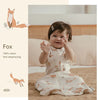 A baby wearing a white and orange patterned cotton vest sleeping bag on a brown blanket.