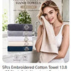 A woman holds a light beige embroidered cotton hand towel in a bright bathroom setting.
