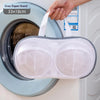 A hand is placing a gray zipper stand mesh laundry bag into a washing machine drum.