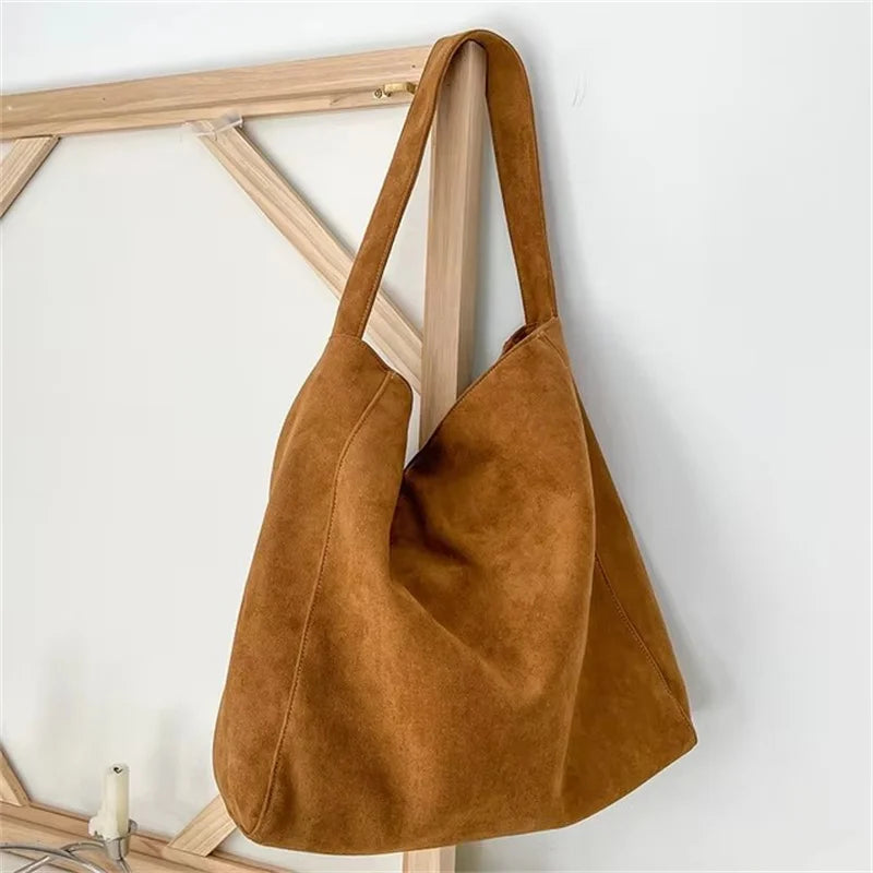 A brown suede tote shoulder bag hanging on a wooden rack.