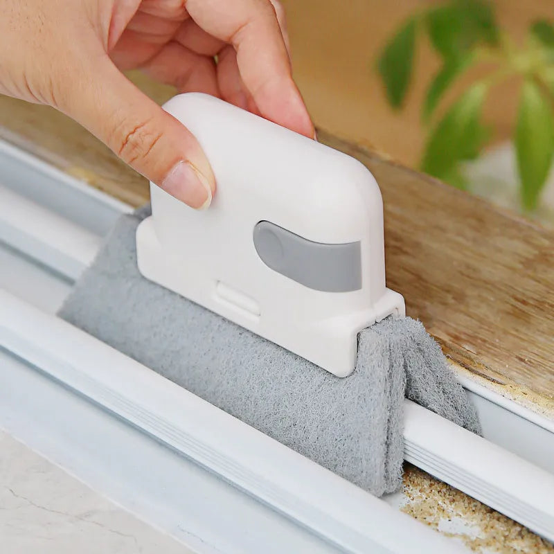 A hand is using a white groove cleaning brush to wipe a window track with a gray cleaning cloth.
