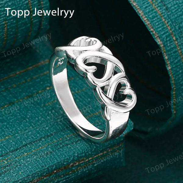Bague en forme de cœur creux argentée sur fond vert foncé.