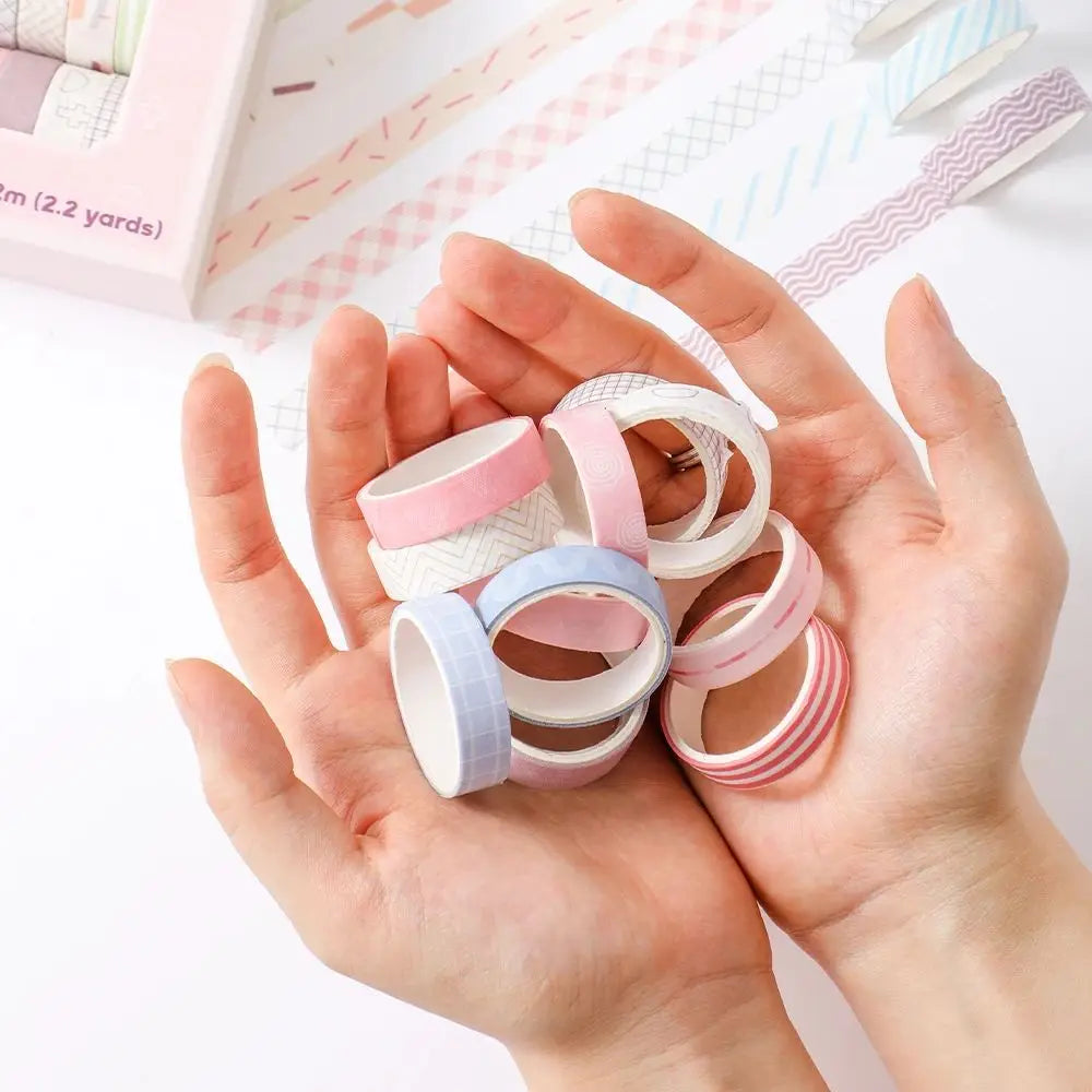 A hand holds a set of colorful washi tape rolls in various pastel shades for journaling and crafts.