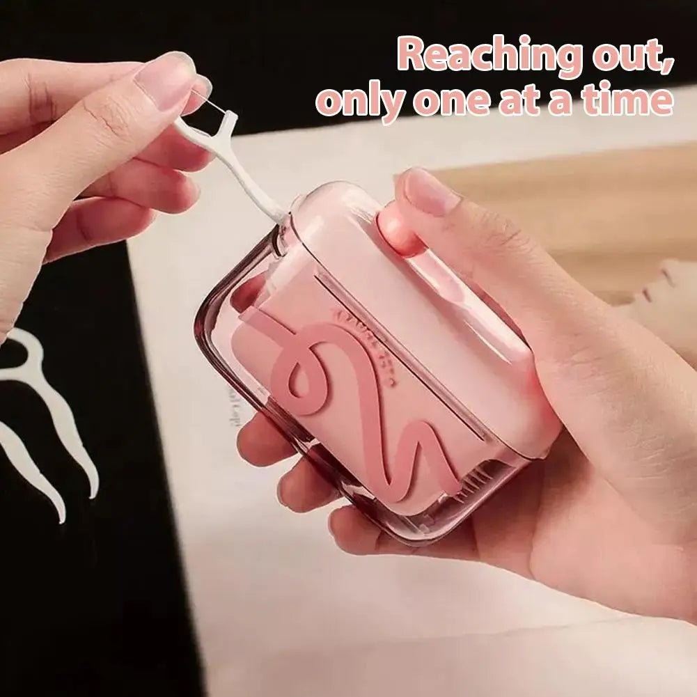 A hand is using a portable automatic floss pick dispenser with a white tool to extract floss.