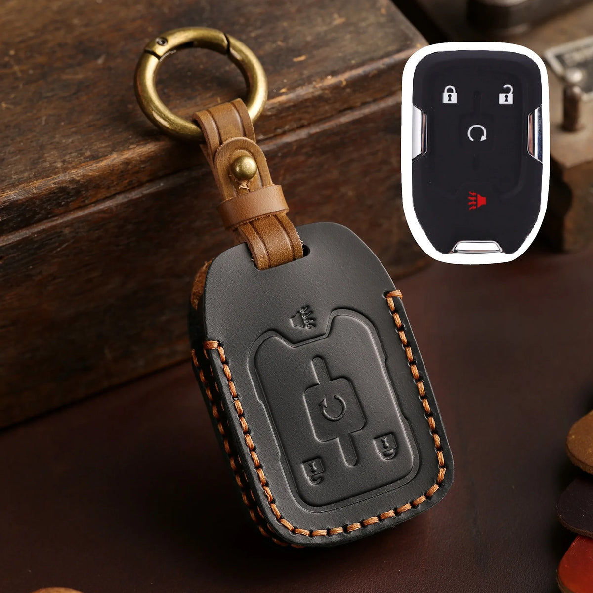 A black leather key fob case with a brass ring attached, next to a white electronic device.