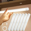 A hand is illuminating a row of white LED light bars, which are motion sensor night lights with USB rechargeable batteries.