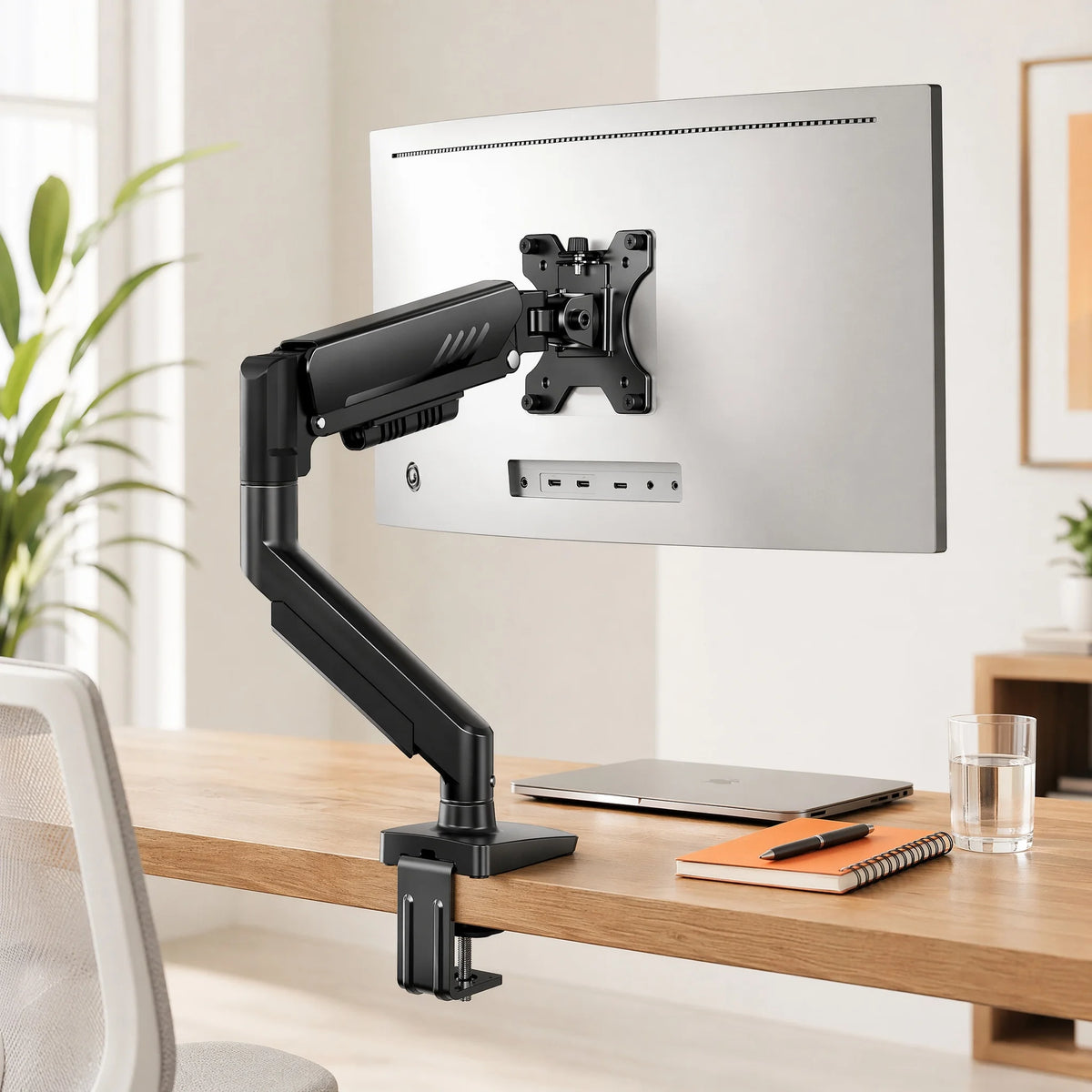 Bras d'écran réglable noir robuste monté sur un bureau en bois, à côté d'un moniteur informatique.