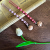 A silicone pacifier clip with a teether made of pink and purple beads rests on an old paper background.