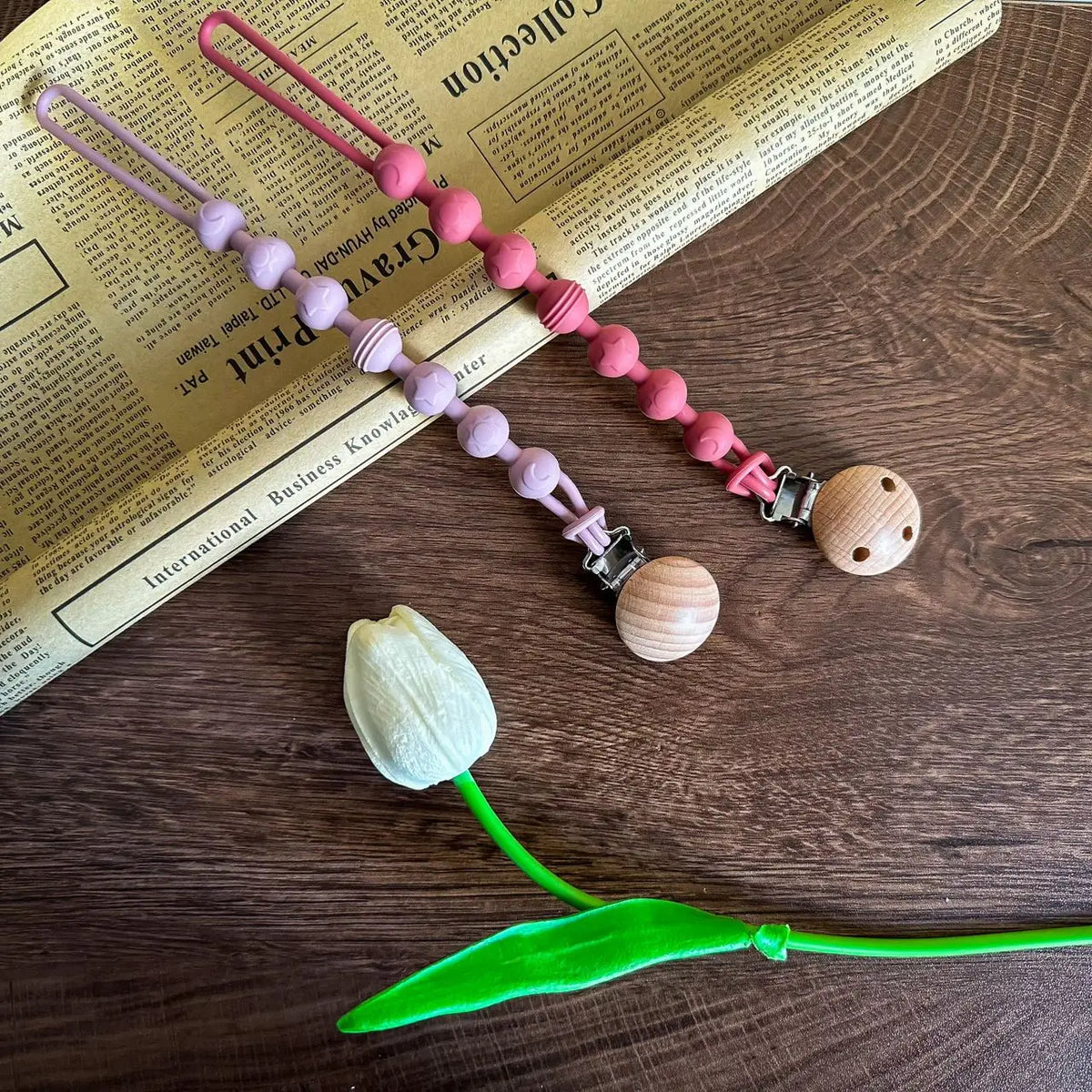 A silicone pacifier clip with a teether made of pink and purple beads rests on an old paper background.
