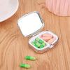A portable metal pill organizer with a hinged lid is shown open, displaying several pink and green pills on a wooden surface.