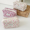 Three floral quilted makeup bags in pink and green patterns are displayed on a woven basket.