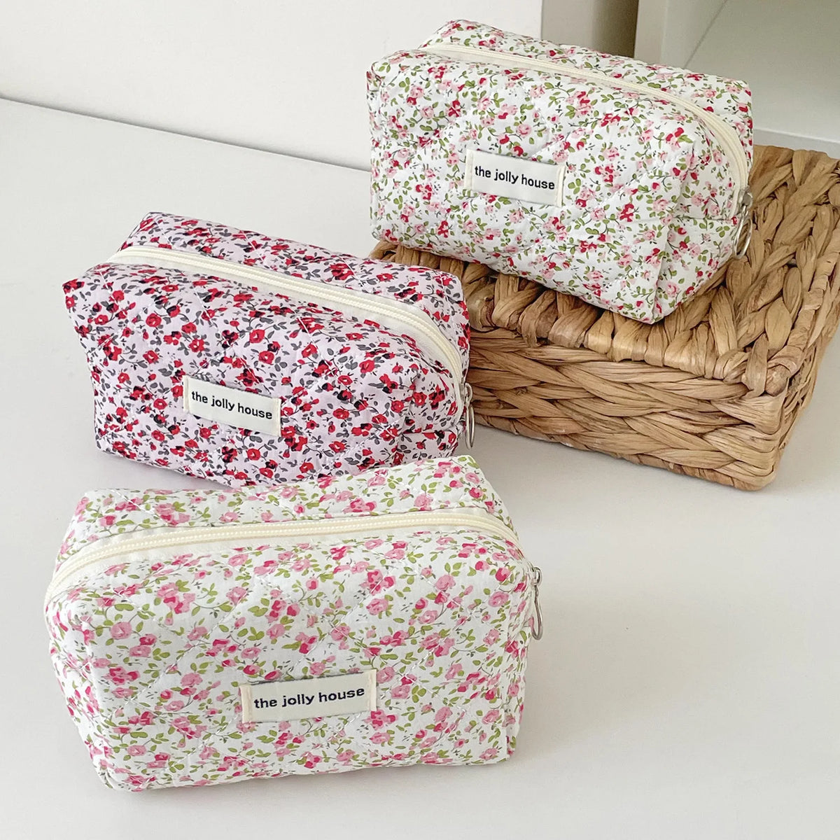 Three floral quilted makeup bags in pink and green patterns are displayed on a woven basket.