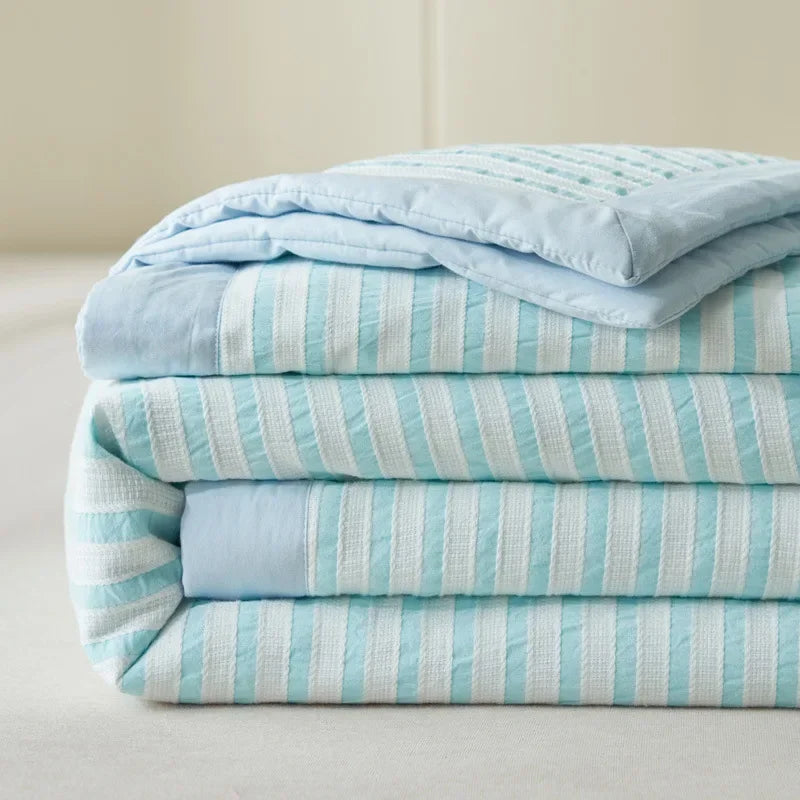 A stack of light blue and white striped breathable summer quilts with jacquard cotton covers.